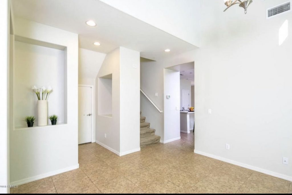 wide angle of a living room space with beige floors and plain white walls
