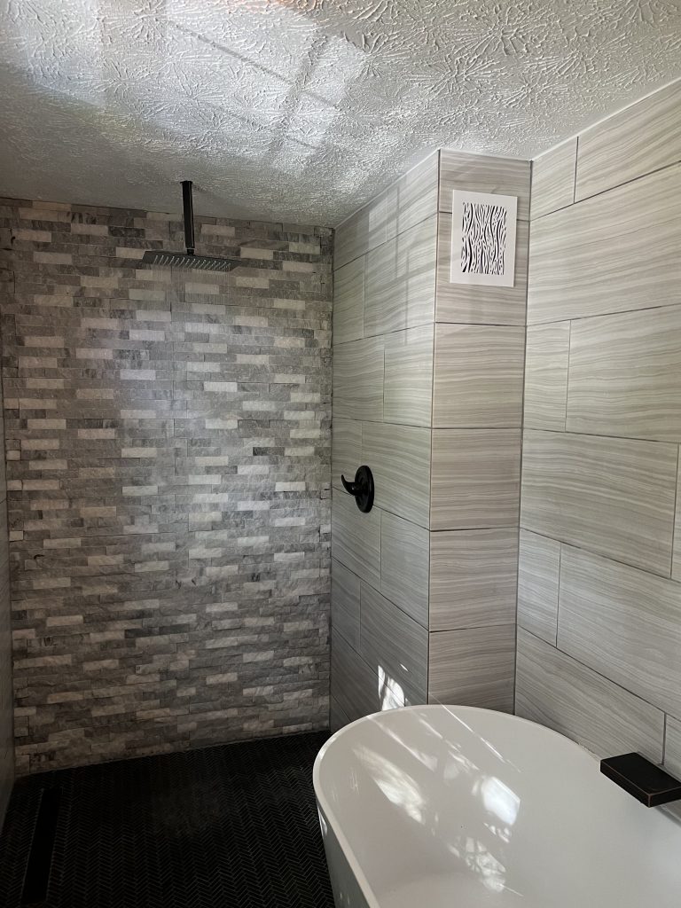 a new wet room style bathroom featuring a rain shower and soaker tub and grey tiled walls and flooring
