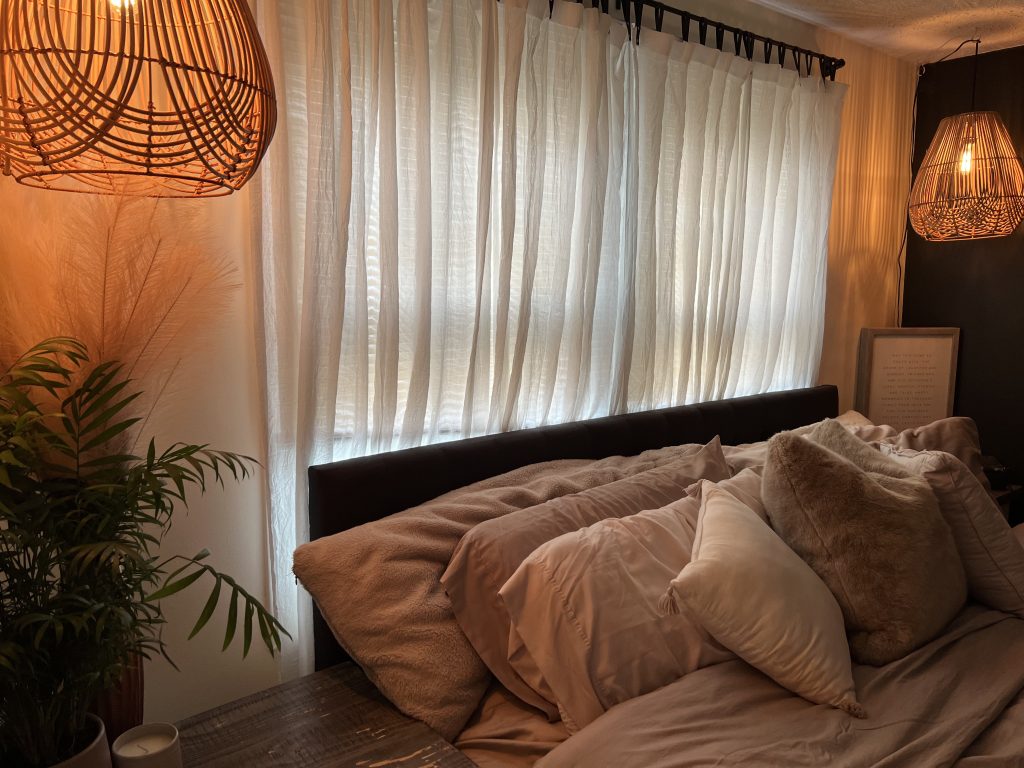 a beautiful window with draped sheer curtains and linen bedding