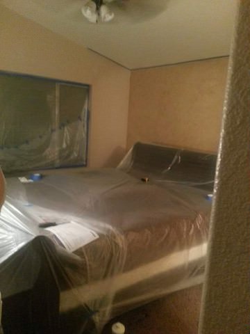 view of a queen bed draped in plastic sheeting in a bedroom with walls faux finished in a peach color